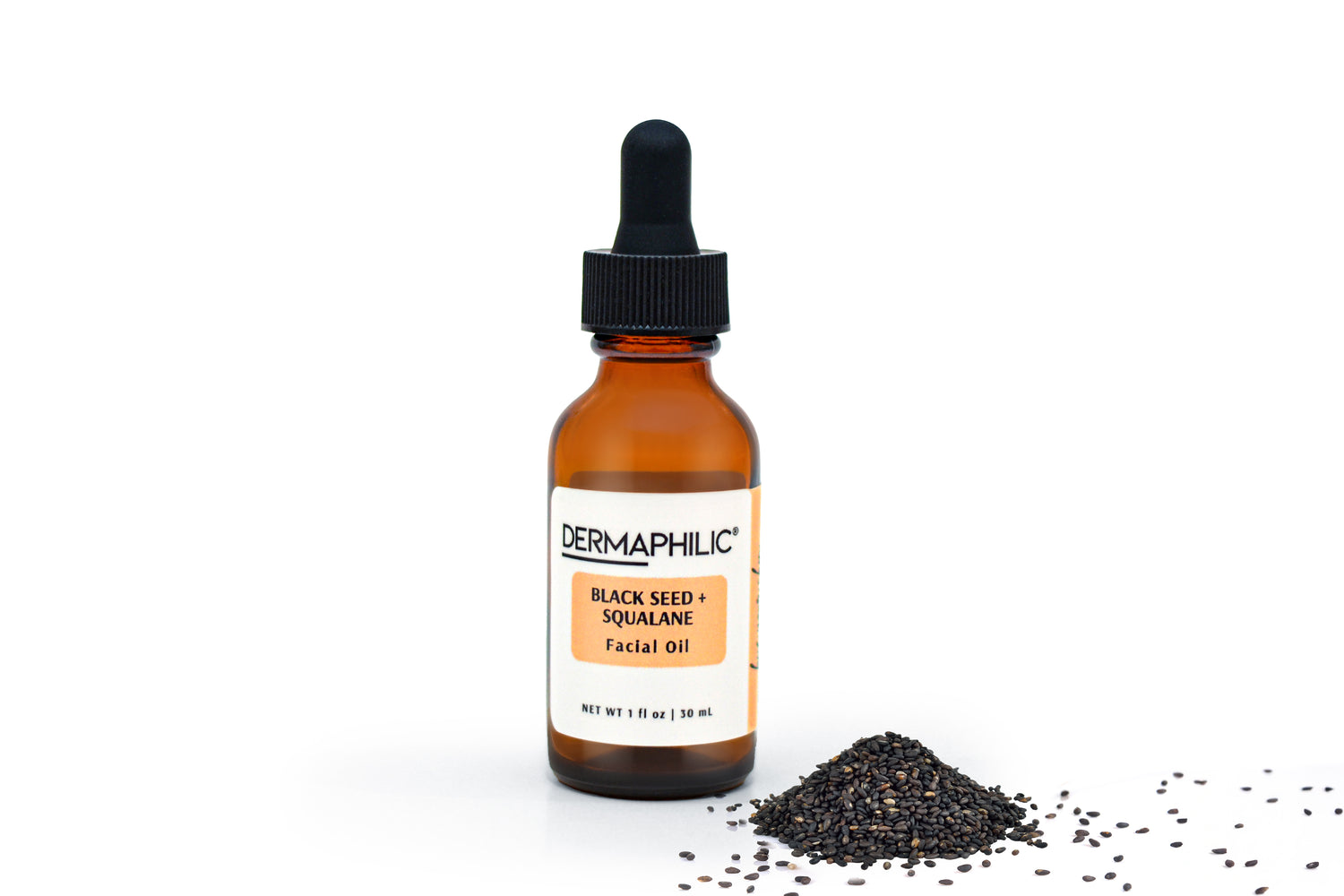 Amber glass bottle with dropper labeled 'Dermaphilic black seed and squalane facial oil' and black seeds piled beside bottle on a white background